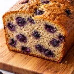 Moist banana bread loaf studded with fresh blueberries suspended throughout, not sunk to the bottom, with a golden brown crust.
