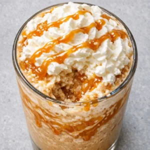 Tall glass of creamy caramel frappuccino with whipped cream and caramel drizzle, ice and blended coffee visible.