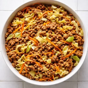 Shredded cabbage and carrots with seasoned ground pork in a bowl, topped with green onions and sesame seeds, glossy with sauce.