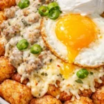 Crispy tater tot breakfast bowl with rich sausage gravy, sunny-side egg, and melted cheddar cheese on a white plate.