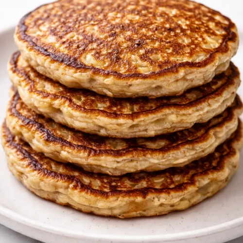 Stack of fluffy 3 ingredient banana oatmeal pancakes with golden brown edges, drizzled with maple syrup, on a white plate.