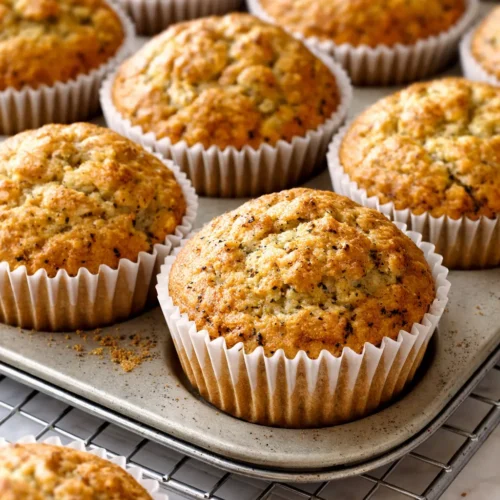 Moist banana zucchini muffins with golden tops and visible green zucchini flecks, piled on a wooden board