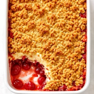 Fresh strawberries and cream cheese filling layered in a baking dish, topped with yellow cake mix and pats of butter for a buttery strawberry cheesecake dump cake.
