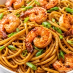 Glistening lo mein noodles with succulent shrimp, crisp red bell peppers, and snap peas, garnished with sliced green onions, coated in a savory glossy sauce.