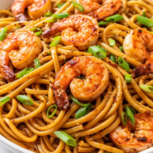 Glistening lo mein noodles with succulent shrimp, crisp red bell peppers, and snap peas, garnished with sliced green onions, coated in a savory glossy sauce.