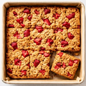 Healthy strawberry oatmeal bars mixture pressed into a baking pan with sticky oats and fresh strawberry chunks, golden and vibrant.