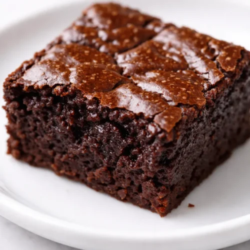 Fudgy high protein brownie bites with rich dark chocolate color and a shiny, cracked top on a white plate.