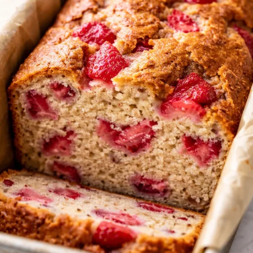 Moist high-protein strawberry loaf with fresh strawberry pieces and a tender crumb, sliced on a rustic wooden board.