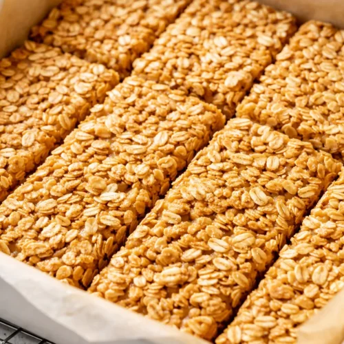 Homemade no bake granola bars stacked neatly, golden brown with visible oats and almonds, chewy texture holding together perfectly.