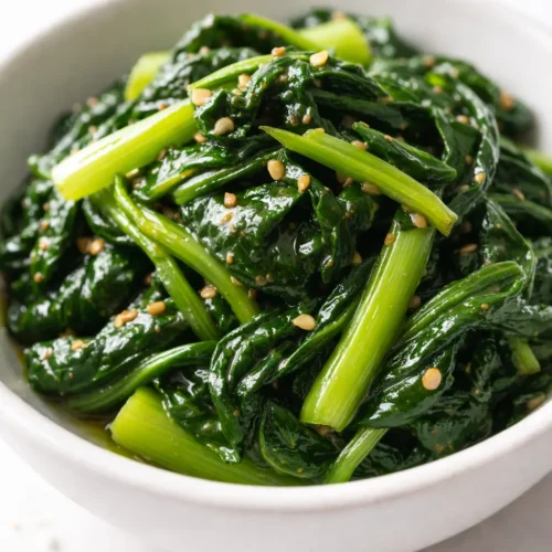 Bright green blanched spinach tossed with sesame oil, toasted sesame seeds, and minced garlic in a white ceramic bowl