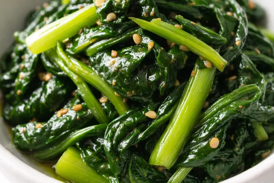 Bright green blanched spinach tossed with sesame oil, toasted sesame seeds, and minced garlic in a white ceramic bowl