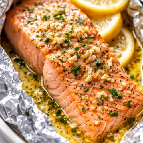 Flaky lemon garlic butter baked salmon in foil, golden brown with a glossy garlic butter sauce and fresh herbs.