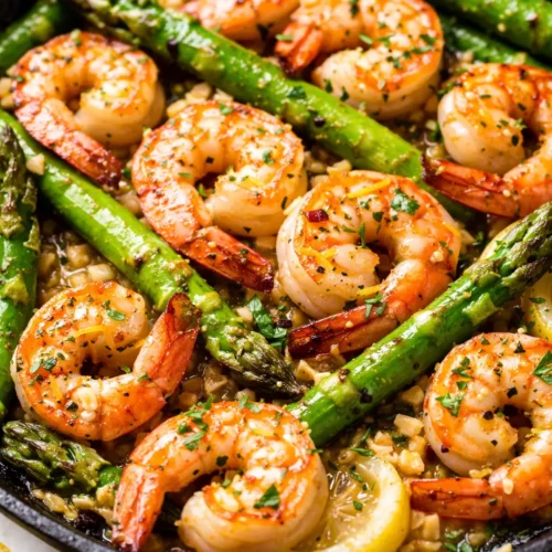 Plump lemon garlic shrimp and tender asparagus spears tossed in a zesty lemon butter sauce on a white plate.