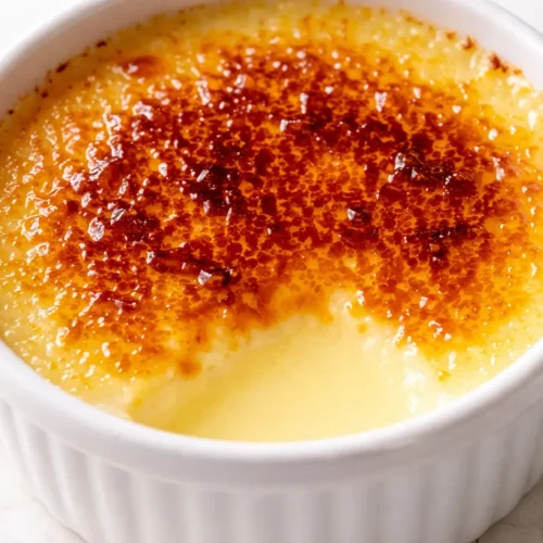 Smooth lemon posset brûlée with a caramelized sugar crust, creamy yellow custard visible in a white ramekin.