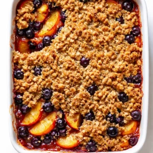 Golden-brown peach and blueberry crisp with brown butter crumb topping in a baking dish, bubbling around the edges
