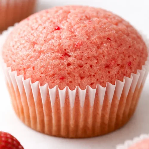 Strawberry cupcakes topped with pink buttercream frosting and a fresh strawberry slice, showing moist crumb and real berry specks.