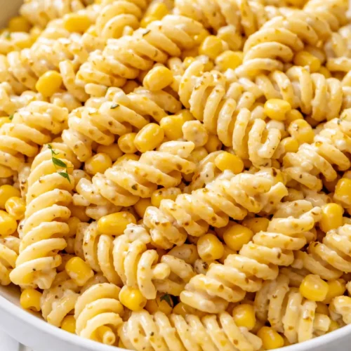 Creamy street corn pasta salad in a white bowl with charred corn kernels, crumbled cotija cheese, fresh cilantro, and a sprinkle of chili powder.