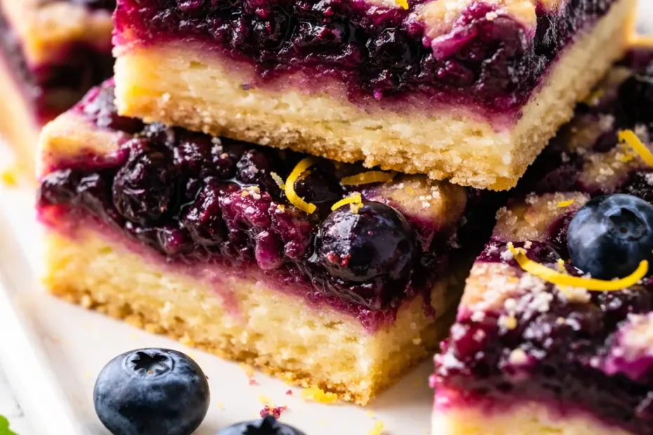 Blueberry lemon pie bars with golden crumble topping, fresh blueberries, and a drizzle of lemon glaze on a white plate.
