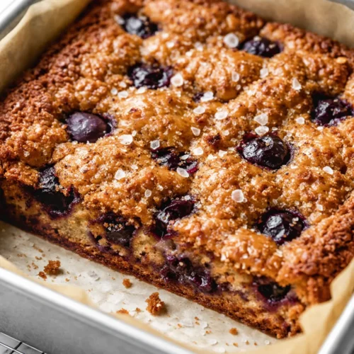 Freshly baked cozy blueberry blondies, golden edges, soft center with juicy blueberries, on a rustic plate.