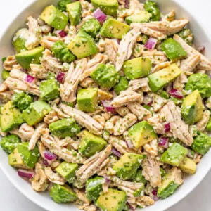 Creamy avocado chicken salad with chunks of avocado and chicken, garnished with fresh herbs, showing its smooth texture and vibrant green color.
