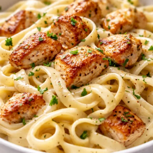Creamy chicken alfredo pasta with golden chicken pieces, rich white sauce, and fresh parsley on a white plate.