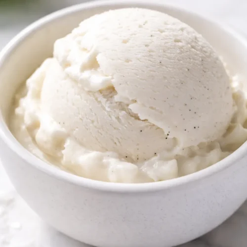 Scoop of creamy coconut ice cream with a smooth, velvety texture and pale white color in a glass bowl.