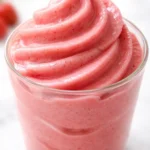 Creamy homemade strawberry Dole Whip in a tall glass, vibrant pink swirl with fresh strawberry chunks, smooth and airy texture.