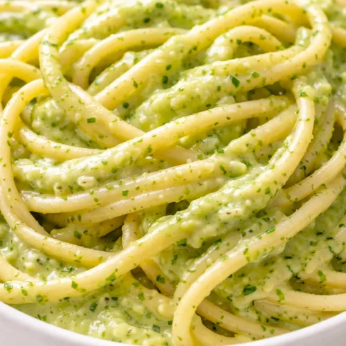 Creamy zucchini sauce with vibrant green ribbons, thick and smooth texture in a white bowl, garnished with fresh herbs