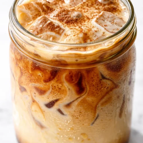 Best French Toast Iced Latte in a clear glass with whipped cream, cinnamon dusting, and caramel drizzle.