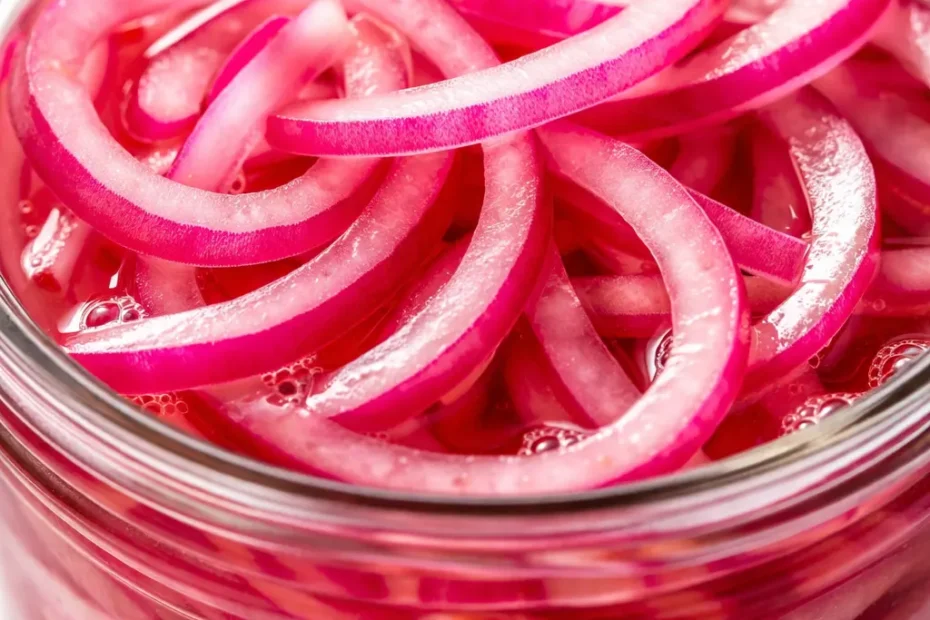 Vibrant magenta pickled red onions in a glass jar, showing crisp translucent slices submerged in tangy brine.