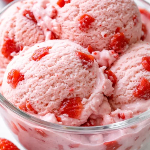 Smooth, creamy homemade strawberry ice cream with visible strawberry pieces, vibrant pink hue, and a rich, velvety texture.