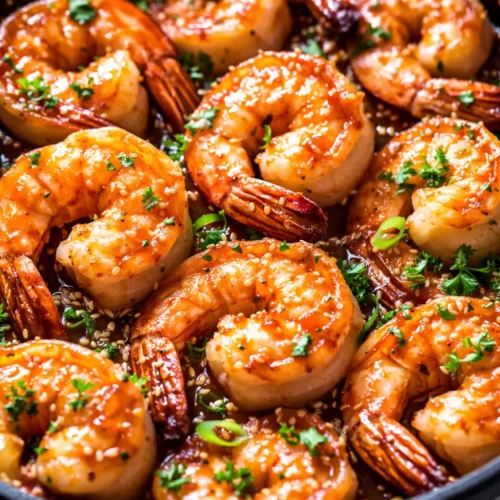 Glossy honey garlic shrimp with golden brown glaze, garnished with green onions and sesame seeds, served on a white plate.