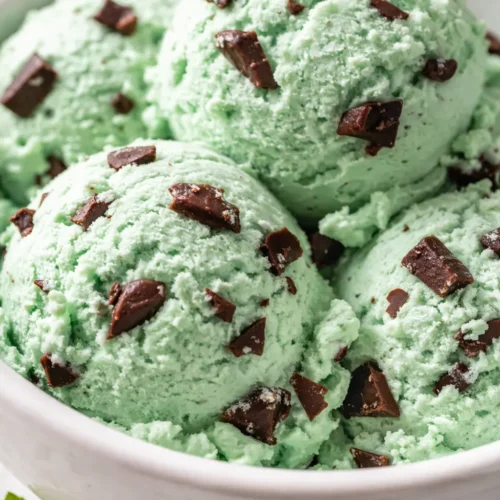 Smooth, scoopable mint green no-churn mint chocolate chip ice cream with dark chocolate chips, in a chilled bowl.
