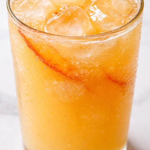 Golden peach lemonade with ice and fresh peach slices, a refreshing summer drink perfect for hot days.