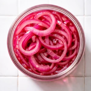 Thinly sliced red onions with vibrant purple color and crisp texture, ready for pickling.