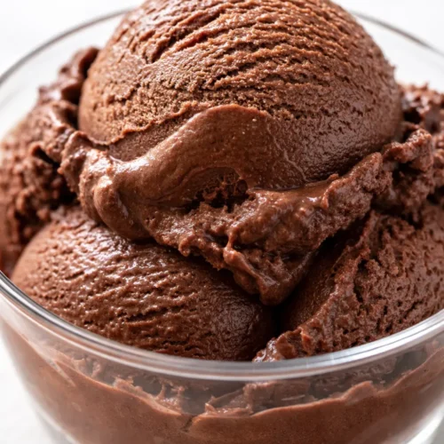 Silky homemade chocolate ice cream in a glass bowl, smooth and creamy texture, rich dark brown color.