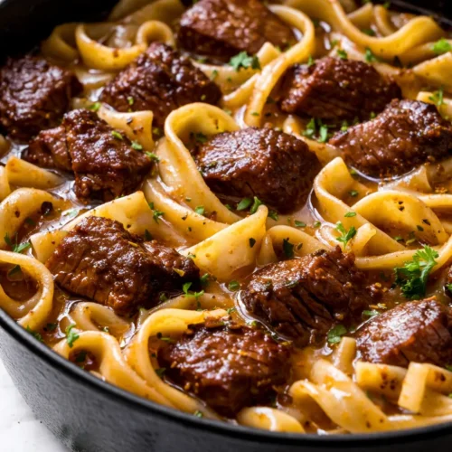 Bowl of slow-simmered beef and noodles with tender beef chunks, thick egg noodles, and rich brown broth garnished with fresh parsley
