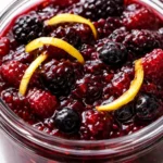 Small batch summer berry jam with perfect set, deep ruby red color, glossy texture, spoonful in a mason jar.