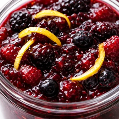 Small batch summer berry jam with perfect set, deep ruby red color, glossy texture, spoonful in a mason jar.