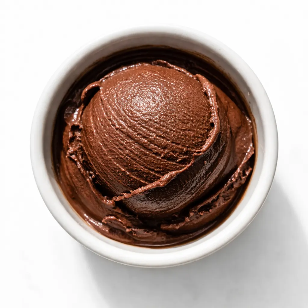 Pouring smooth dark chocolate gelato mixture into a container, showcasing its rich brown color and silky slow-melt texture.