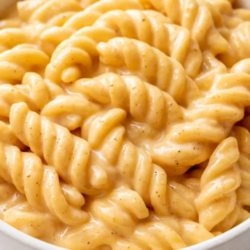 Creamy spicy pasta sauce coating fettuccine, with red chili flakes and fresh basil, rich orange hue.