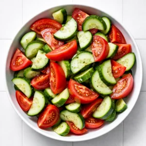 Fresh cucumber slices and halved cherry tomatoes in a bowl with light vinaigrette, crisp vegetables for a summer salad.