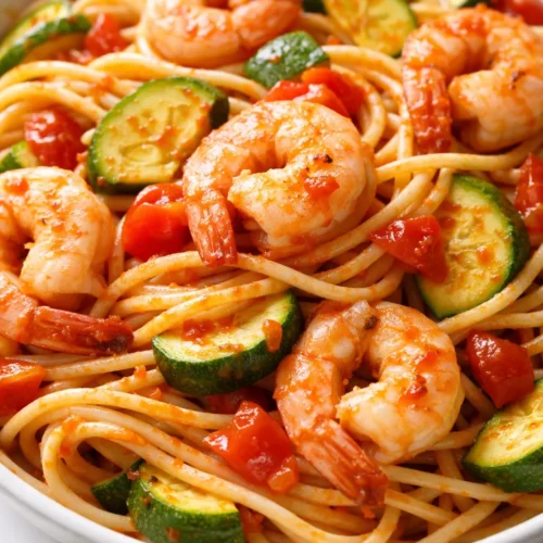 Plate of tomato zucchini shrimp pasta with tender shrimp, zucchini slices, and cherry tomatoes in a light sauce, garnished with fresh parsley.