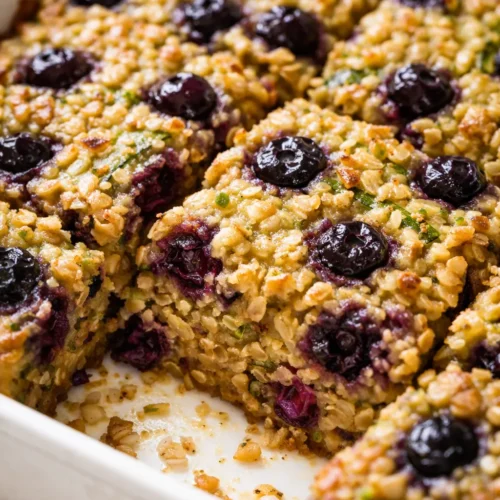 Warm golden baked oatmeal with blueberries and shredded zucchini, topped with fresh berries and a light dusting of cinnamon.