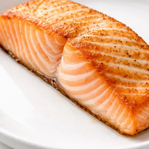 Air fryer salmon with golden-brown crust and tender, flaky pink flesh, garnished with lemon and fresh dill.