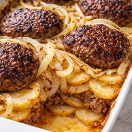 Hearty Amish hamburger steak bake in a cast iron skillet with golden melted cheese, savory brown gravy, and tender beef patties, garnished with parsley.