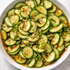 Hands squeezing excess water from salted cucumber slices to keep Asian cucumber salad crunchy and never watery.