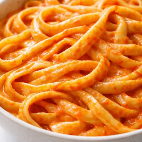 Creamy red pepper alfredo sauce coating fettuccine pasta with vibrant orange color and smooth velvety texture