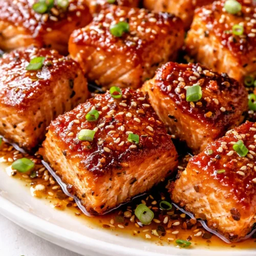 Golden crispy honey garlic salmon bites glazed in glossy sauce, garnished with sesame seeds and green onion.