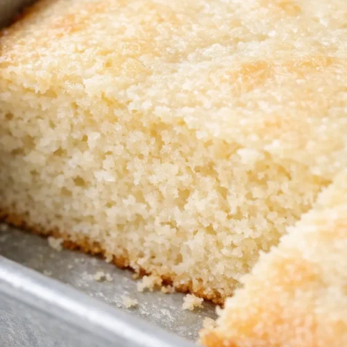 Fluffy vanilla sheet cake with golden-brown edges and creamy white frosting, soft buttermilk crumb visible on a slice.